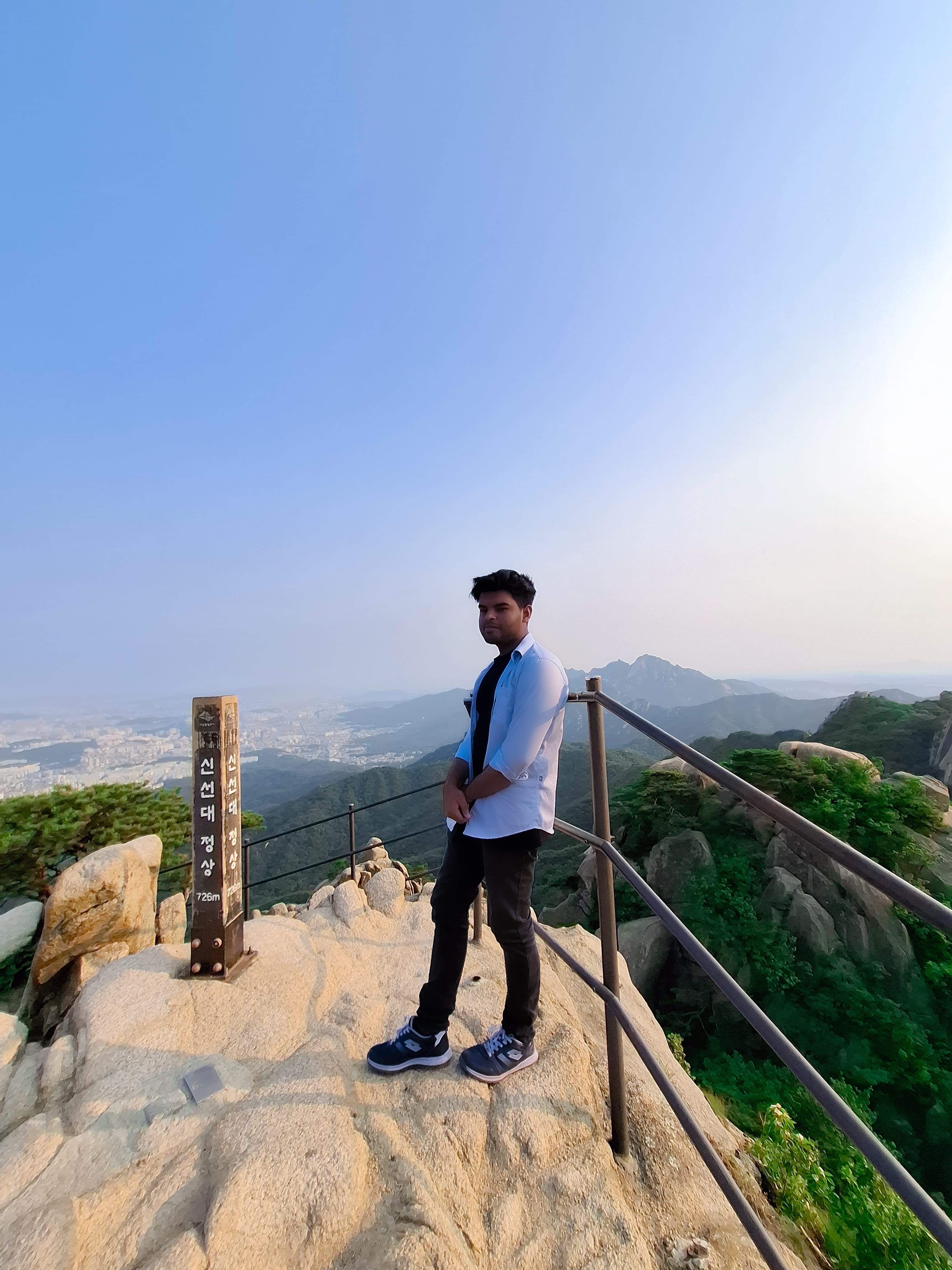Shawkat Hossain Maruf at the peak of Dobongsan Mountain in South Korea, looking over the cityscape at sunset.